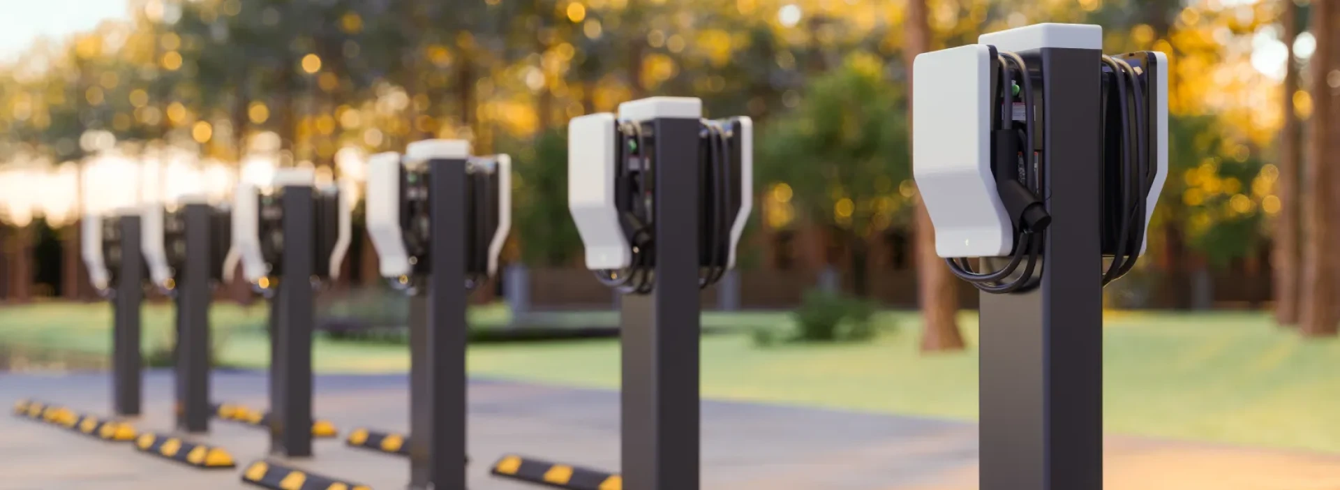 A group of modern looking EV chargers in an outdoor parking area with trees in the background.