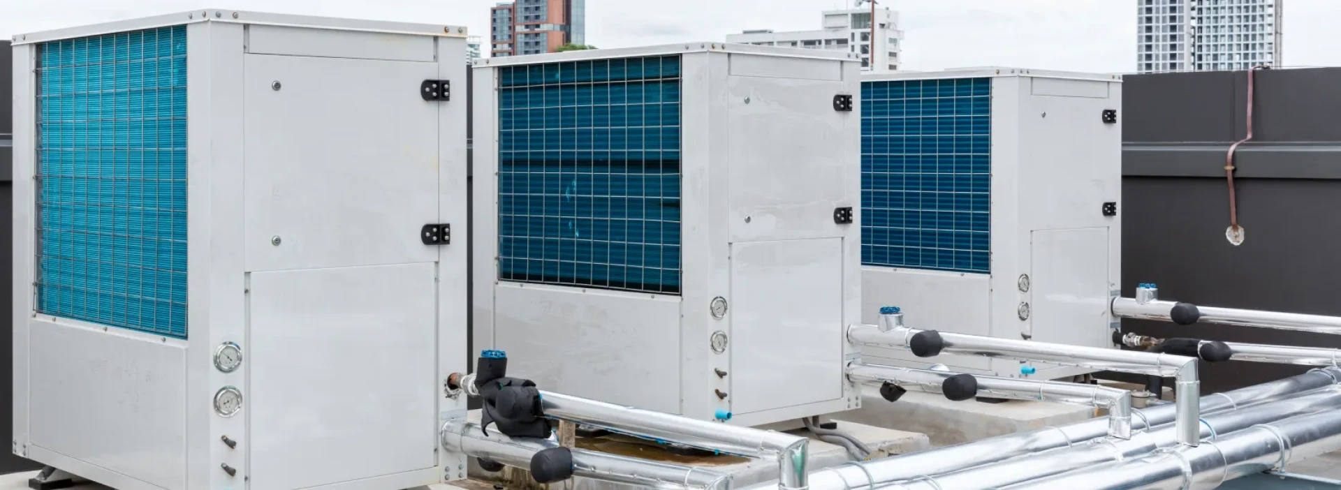 Industrial air conditioner compressor installed on roof building, with skyscrapers in the background.