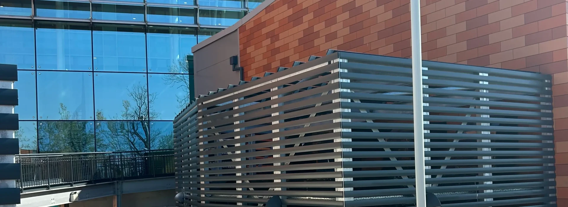 Large cage with commercial heat pumps in it at the side of the hospital by a red brick wall.