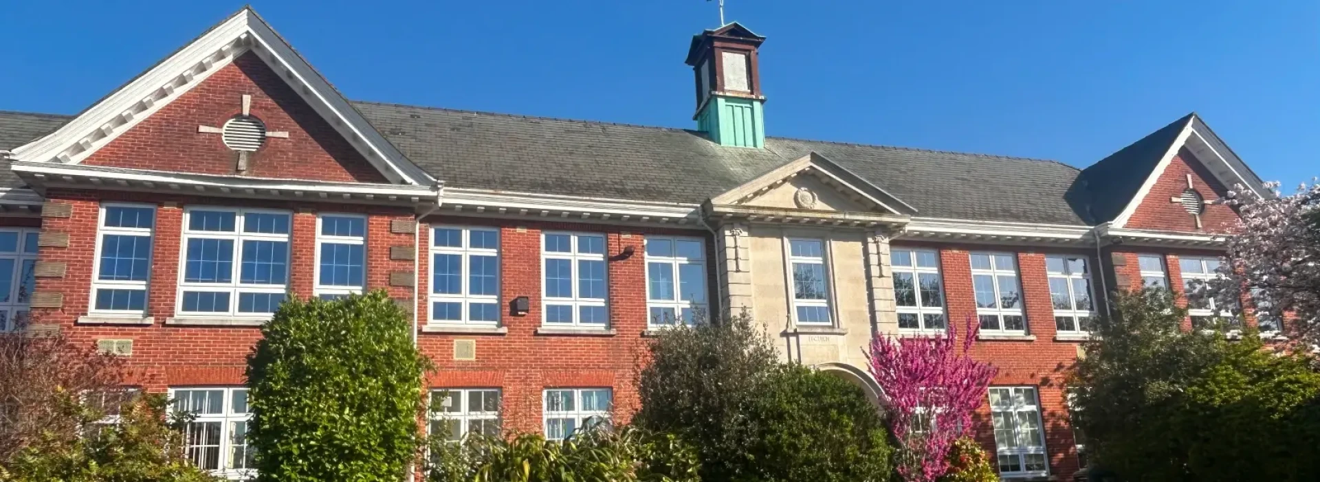 Itchen college building front on a sunny day, with trees and small turret for weathervane.