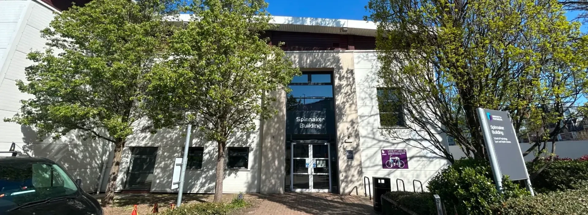 The Spinnaker Building entrance at the University of Portsmouth, on a sunny day with green trees around it.
