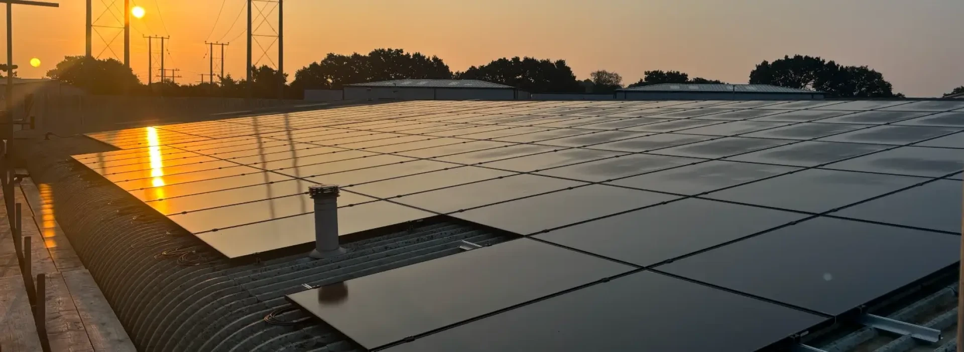 A large industrial roof with many solar panels, and the sun setting in the background.