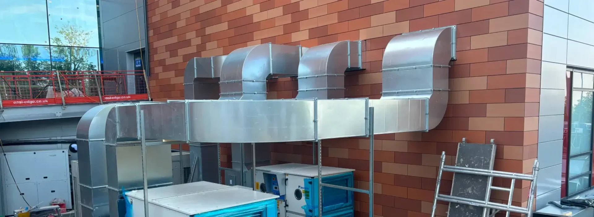 Silver coloured ductwork coming out of the outside of a red brick building.