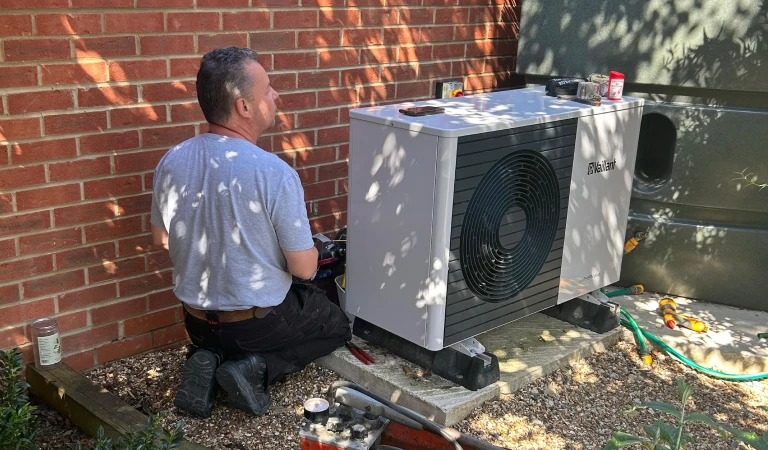 Andy installing a Vaillant heatpump in a sunny garden, against a red brick wall.