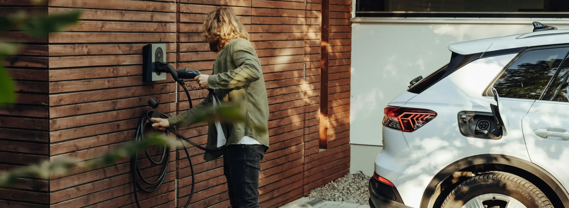 A person using a wall mounted home EV charger, with their white car.