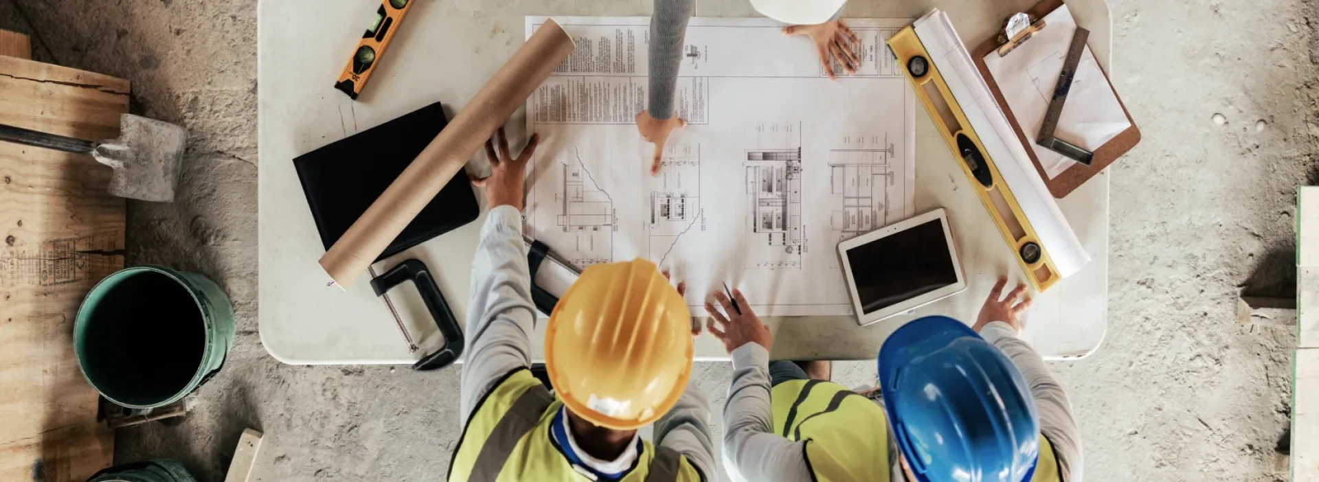 Overhead view of people around a table discussing design plans on a construction site.