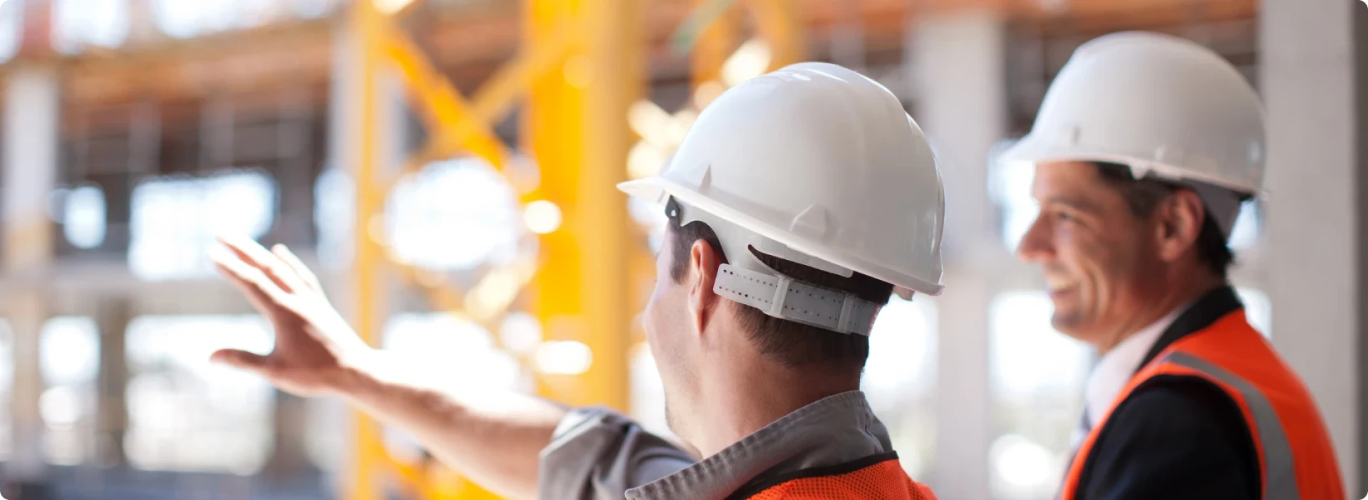 Two people wearing hard hats and high vis vests, on a construction site, discussing a project.