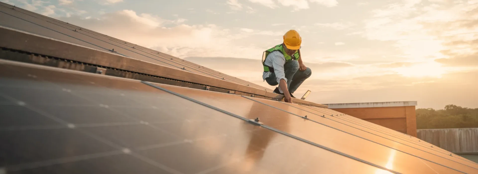 An engineer crouched down on a solar roof, with sun shining in the background.